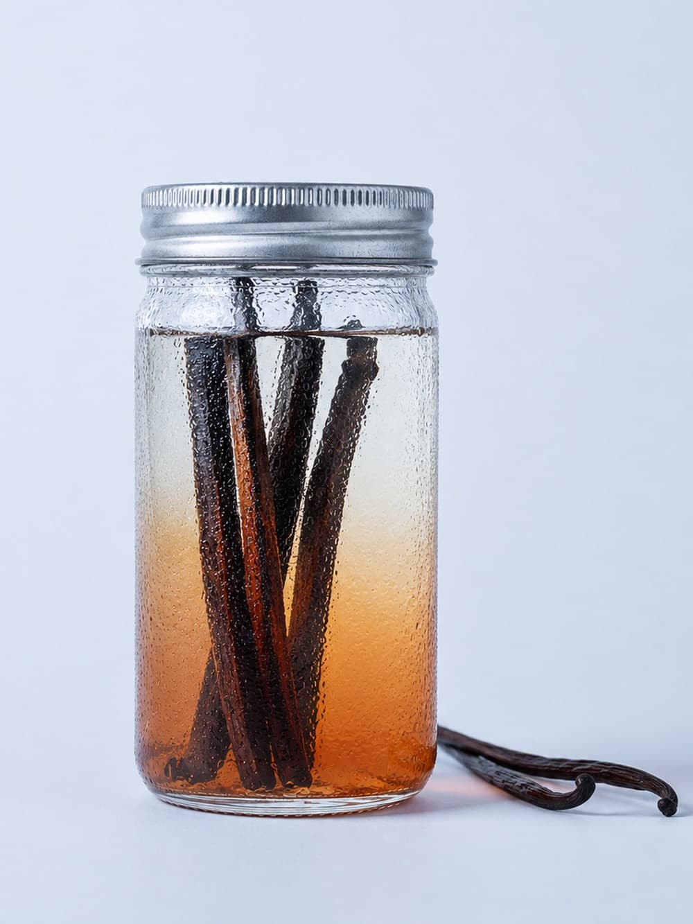 Split vanilla beans steeping in a small jar of clear spirit