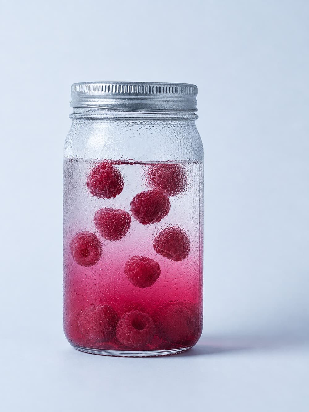 A jar of spirit mid-infusion, fruit suspended in tinted liquid